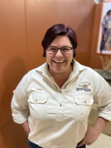 An image of a woman, Trish Sloan, in a cream-coloured workshirt with the Australian Age of Dinosaurs Logo