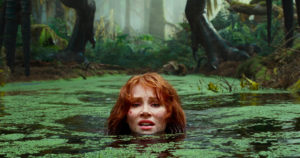 Claire Dearing in swampy water with a dinosaur in the background